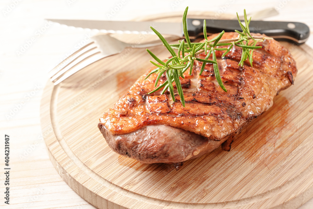 Crispy and juicy duck breast with rosemary garnish on a wooden chopping board with fork and knife, selected focus