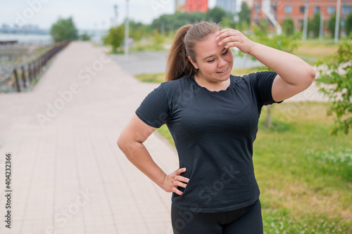 An obese young woman jogging outdoors. Fat beautiful smiling girl in a black tracksuit is engaged in fitness for weight loss on the waterfront. A woman runs on a summer day.