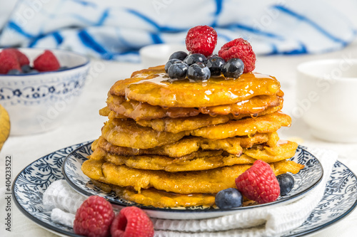 Pile of vegan pancakes with berries and syrup on a blue-white patterned plate on white background