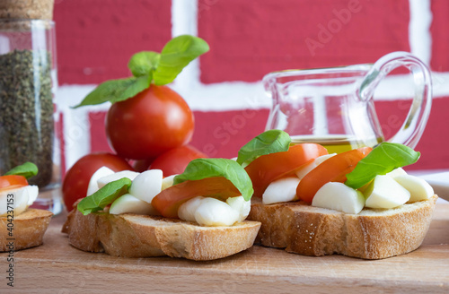 on a wooden stand are crackers with mozzarella, basil, tomatoes near spices and rapeseed oil in a jug photo