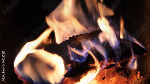 Fire is burning in the fireplace. Warmth and home comfort. Bright fire flames in dark hearth. Looped closeup view of burning wood and red coal