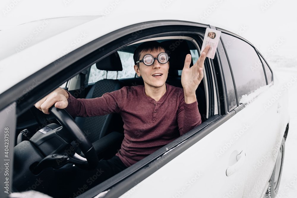 Funny nerd and geek in huge ridiculous glasses shows his drivers license. Concept of police checks on the roads and the correction of vision for drivers