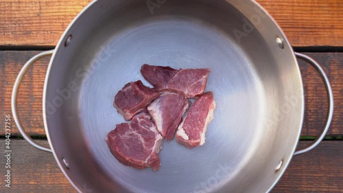 Woman cooking tasty home dinner concept. Top view 4k video of female hand puts many uncooked fresh raw pieces of pork meat fillet on bottom of cooking pot standing on brown wooden table background. photo