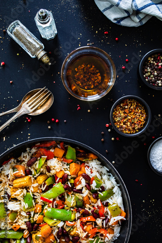 White rice with mix of vegetables in frying pan on black wooden table 