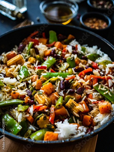 White rice with mix of vegetables in frying pan on black wooden table 