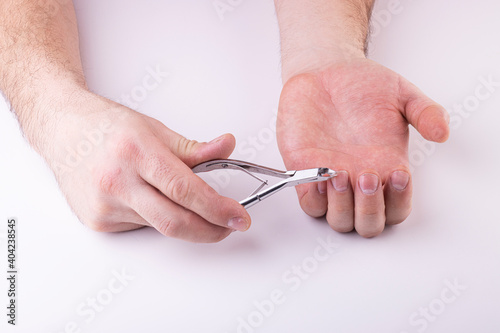 A man s hand holds a nail clipper  trimming the nails on his thumbs  on a white background