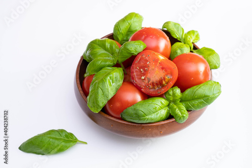 fresh tomatoes and green basil in a wooden cup on a white table