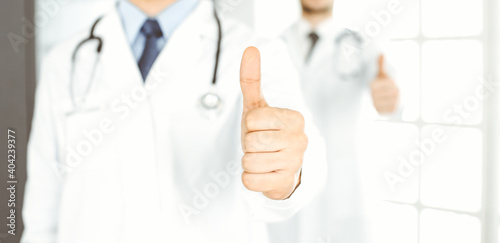 Two male doctors standing as a team with thumbs up in hospital office and ready to help patients. Medical help, best disease treatment and medicine concept