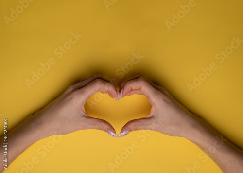 heart making woman s hands with manicure on yellow background  top view