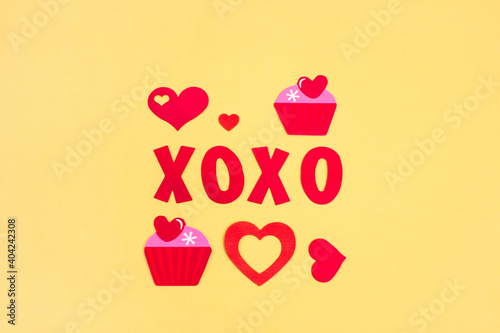 XOXO phrase with heart and cupcakes on bright background. Lettering on romantic theme. 