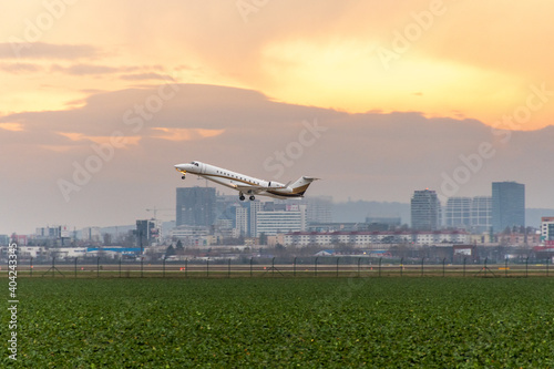 Small white Embraer legacy 600 plane departing from Bratislava airport with gear down with magical orange sky in the background photo