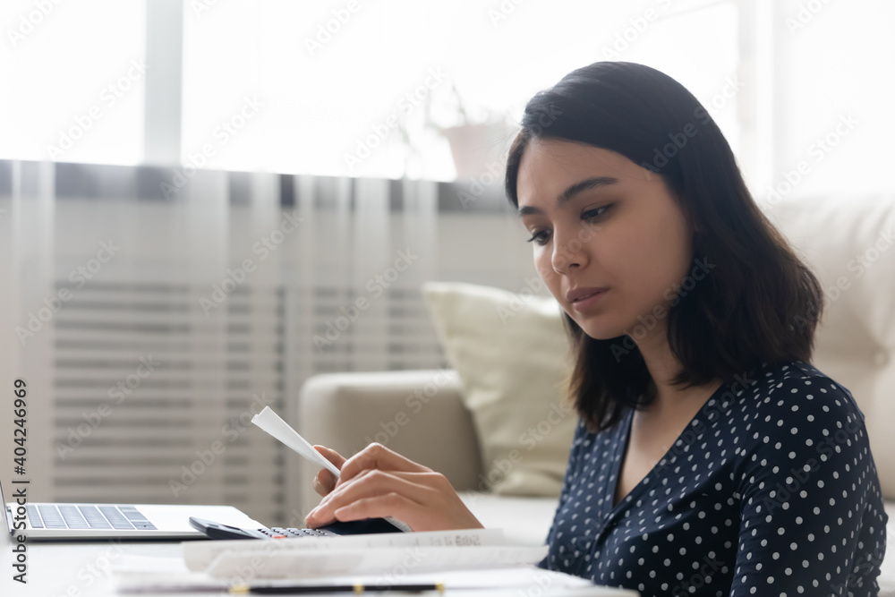 Head shot concentrated young mixed race vietnamese woman busy with domestic financial paperwork, calculating monthly income and expenditures, managing budget or paying taxes utility bills at home. Head shot concentrated young mixed race vietnamese woman busy with domestic financial paperwork, calculating monthly income and expenditures, managing budget or paying taxes utility bills at home.