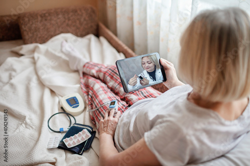 Old woman in bed looking at screen of laptop and consulting with a doctor online at home, telehealth services during lockdown, distant video call, modern tech healthcare application