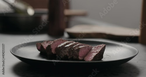 Slow motion orbit shot of sliced beef steak on black plate on concrete countertop photo