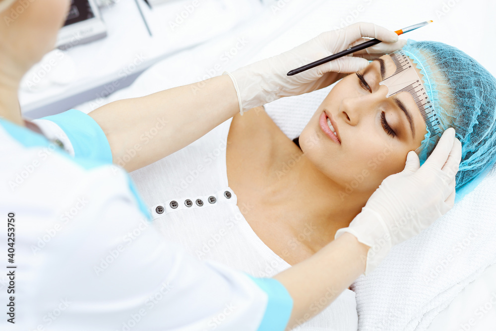 Professional beautician is going to correct eyebrow line at woman face using cosmetic ruler. Permanent brow makeup in beauty salon, closeup. Cosmetology treatment