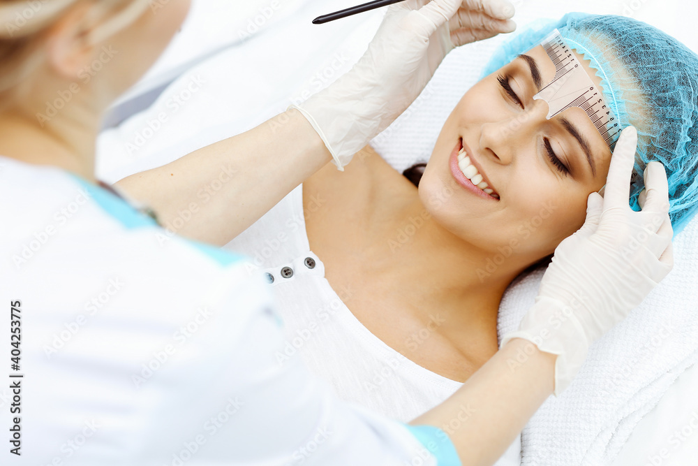 Professional beautician is going to correct eyebrow line at woman face using cosmetic ruler. Permanent brow makeup in beauty salon, closeup. Cosmetology treatment Professional beautician is going to correct eyebrow line at woman face using cosmetic ruler. Permanent brow makeup in beauty salon, closeup. Cosmetology treatment
