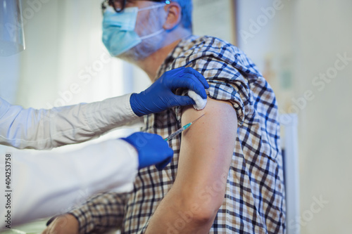 Young woman nurse with surgical mask and face shild giving injection to senior man.