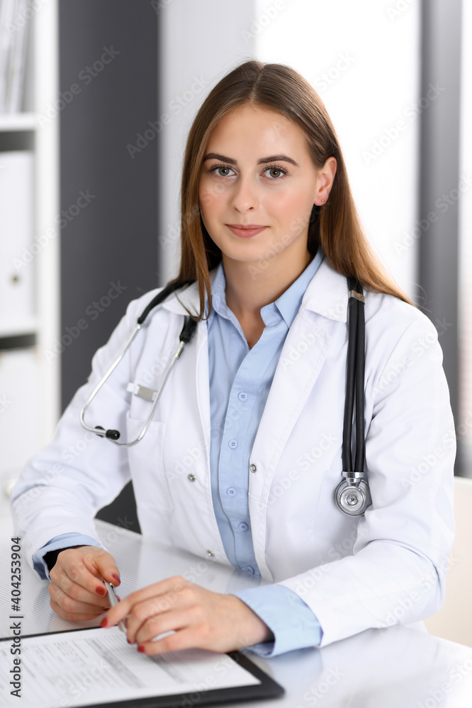 Doctor woman filling up medical form while sitting at the desk in hospital office. Physician at work. Medicine and health care concept Doctor woman filling up medical form while sitting at the desk in hospital office. Physician at work. Medicine and health care concept