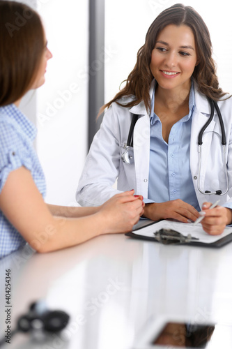 Doctor and happy patient talking while sitting at the desk. The physician or therapist discussing healthy lifestyle. Health care  medicine and patient service concept