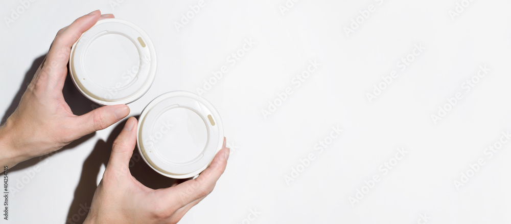Male hands holding disposable cups with coffee on a white background, top view. Banner, copy space. Food delivery concept, coffee to go
