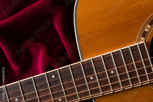 Close up of acoustic guitar on burgundy cloth, fabric, top view