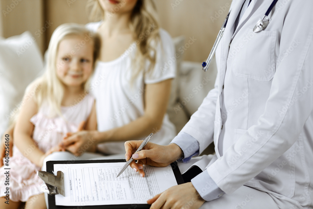 Fototapeta premium Doctor and patient. Pediatrician using clipboard while examining little girl with her mother at home. Happy cute caucasian child at medical exam. Medicine concept