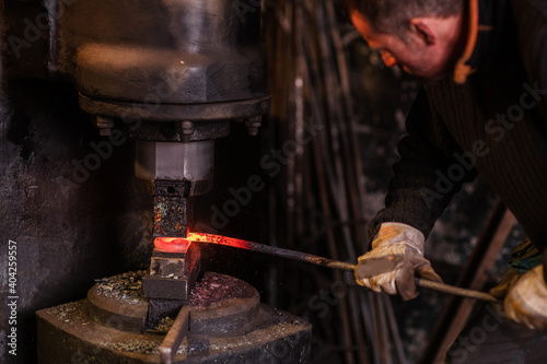 Real brutal blacksmith works in a workshop mechanical hammer with a red-hot iron. Portrait of a profession.
