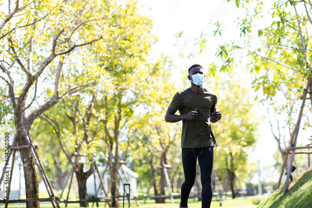 African American Man wearing protective medical face mask jogging and running beside road in park at morning.