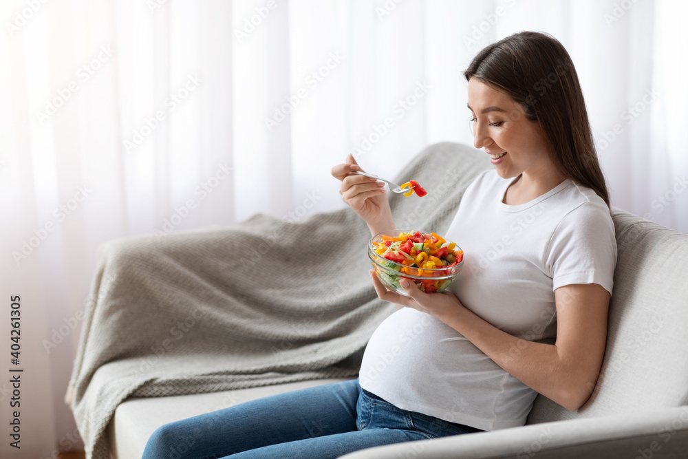 Vitamin Food. Happy Pregnant Woman Eating Vegetable Salad While Sitting On Couch