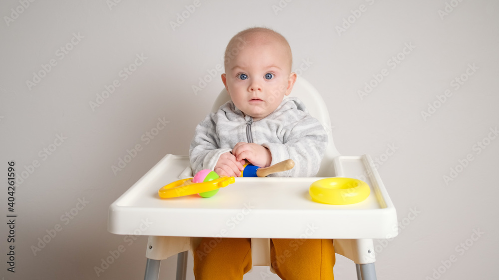 Little baby sitting in high chair playing with toys against grey wall. Little baby sitting in high chair playing with toys against grey wall.