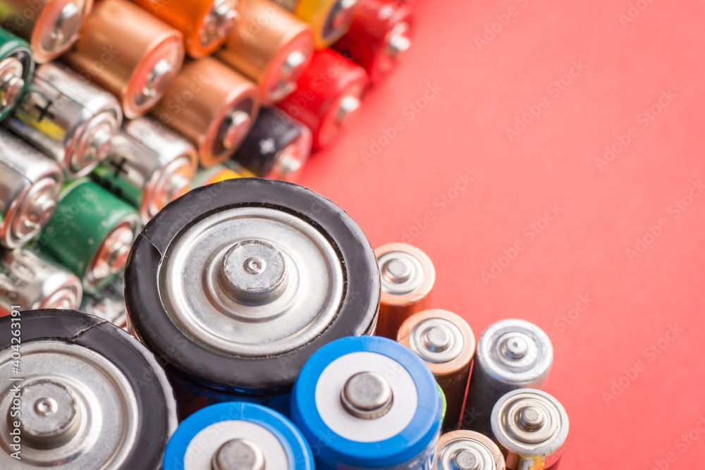 Different batteries on red background. Symbol of recycling rechargeable lithium batteries Different batteries on red background. Symbol of recycling rechargeable lithium batteries