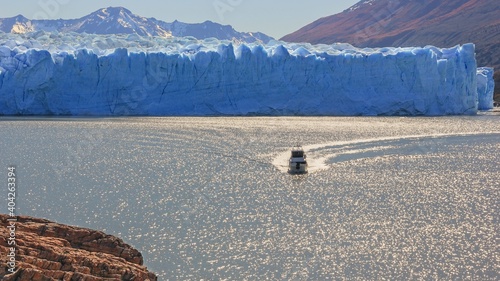 Panoramic view to glacier landscape with tourist boat sailing on dazzle blurred surface of lake in sun glare near famous melting Perito Moreno glacier, in Patagonia, Argentina.