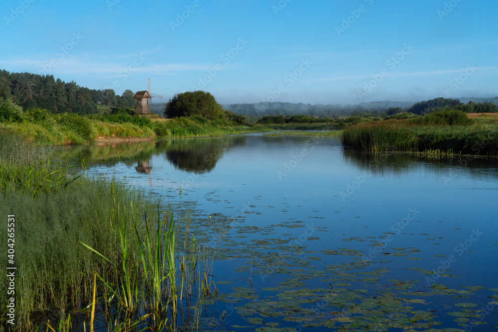 Obraz premium State museum-reserve of Alexander Pushkin. Beautiful russian landscape with an old windmill on the bank of the Sorot river. July 2020.