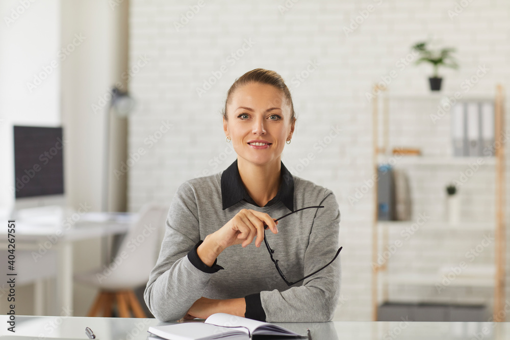 Young smiling woman office worker sitting and looking at camera during business videocall with colleagues and partners in office. Distant working, videocall, teleconference concept Young smiling woman office worker sitting and looking at camera during business videocall with colleagues and partners in office. Distant working, videocall, teleconference concept