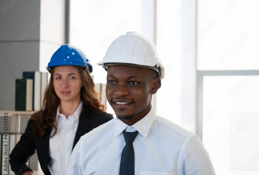 young african american engineer is smiling and standing in office near caucasian woman young african american engineer is smiling and standing in office near caucasian woman