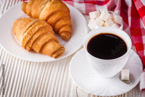 delicious fresh croissant and cup of coffee on a white wooden rustic background