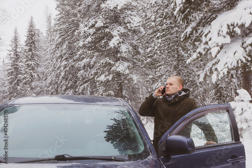 A young man in the winter on the car got lost and talking on the phone getting out of the car. Concept of winter road travel, road search, navigation..