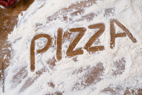Flour and the words pizza are scattered across the table. Ingredient for making Italian pastries.