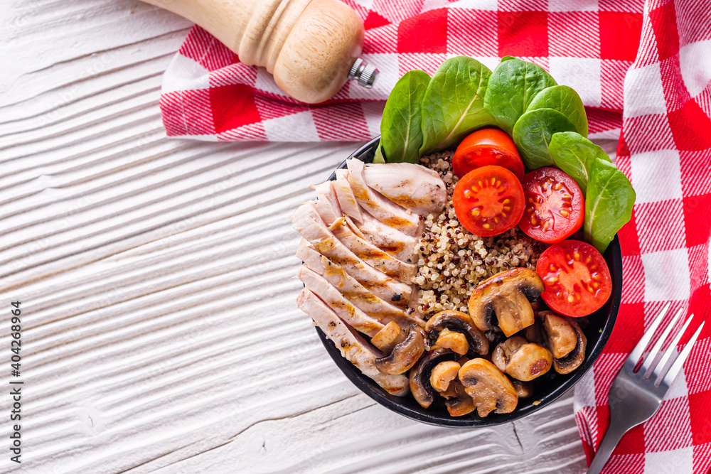 bowl of healthy quinoa with grilled chicken and vegetables on a white rustic wooden background