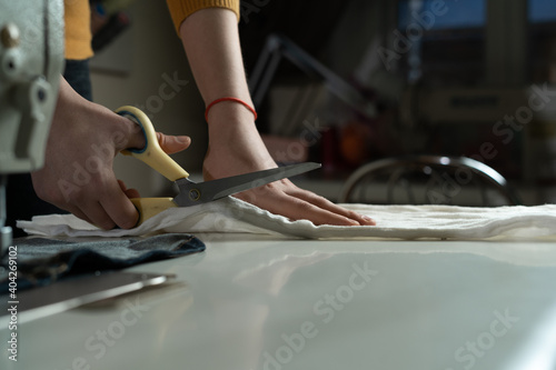 Women's hands cut fabric on a pattern with tailor's scissors on a white table. A dressmaker at work in a sewing studio.