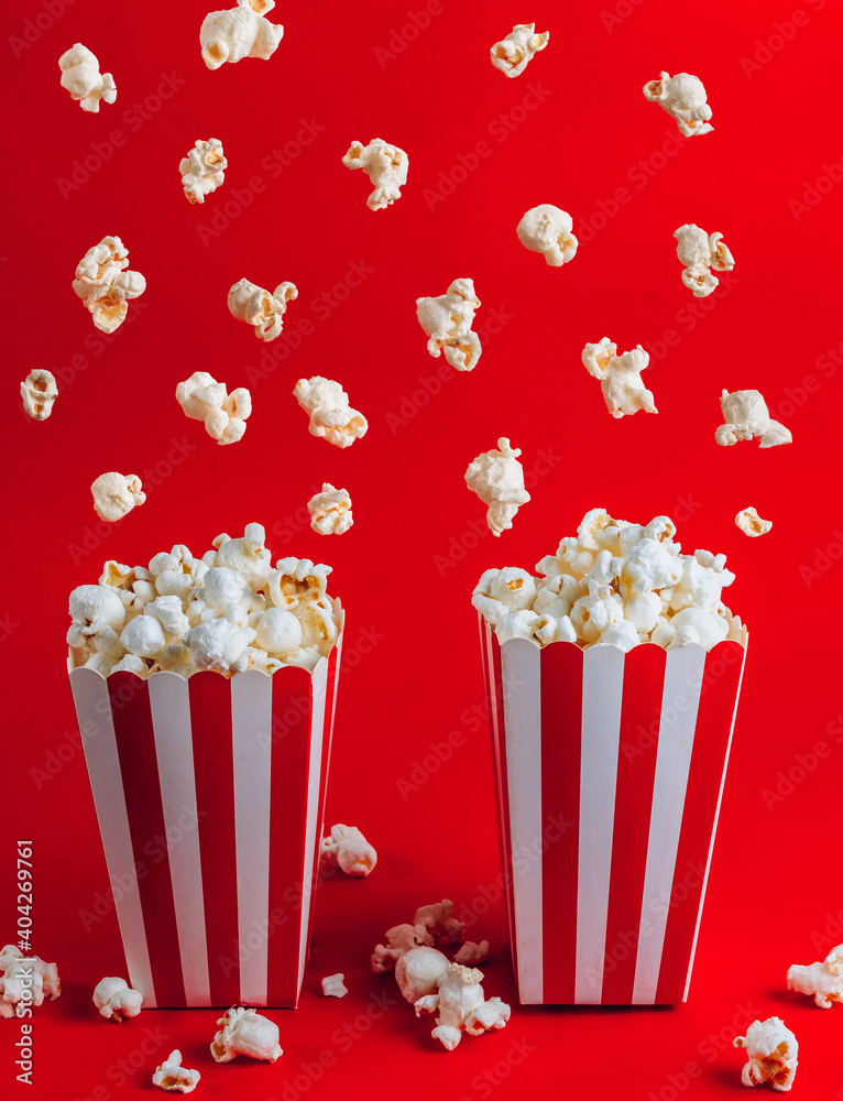 Popcorn falling into a red striped paper cups, on red background