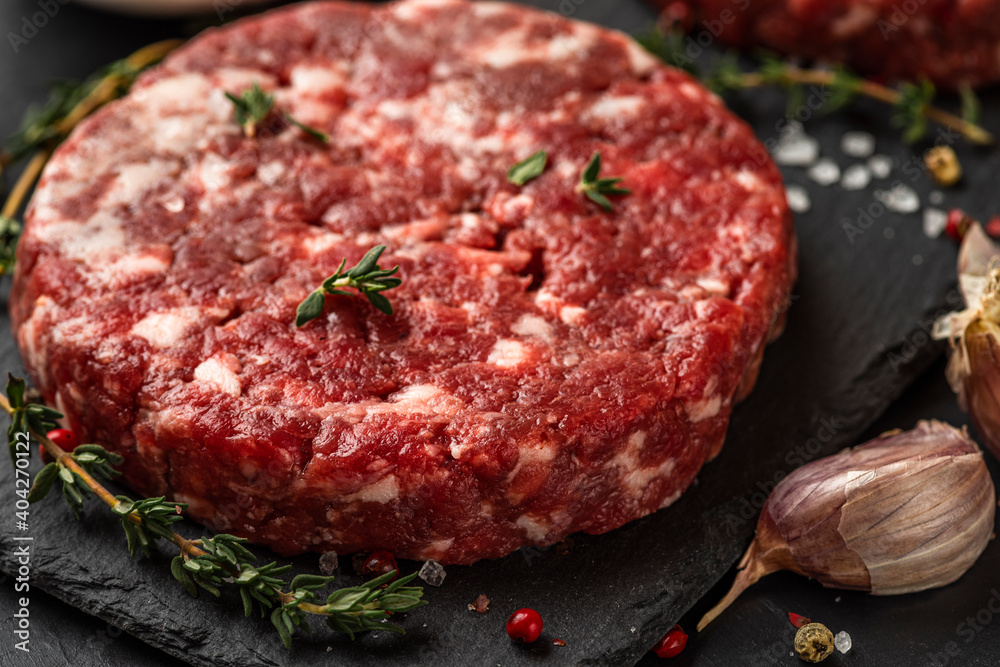 Raw beef hamburger patty or cutlet with herbs and spices for cooking on dark background