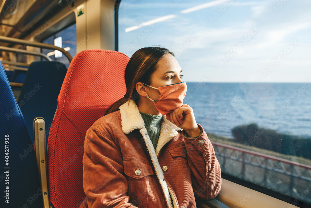 Girl in a protective face mask on the train. Travel by train or suburban trip. - obrazy, fototapety, plakaty 