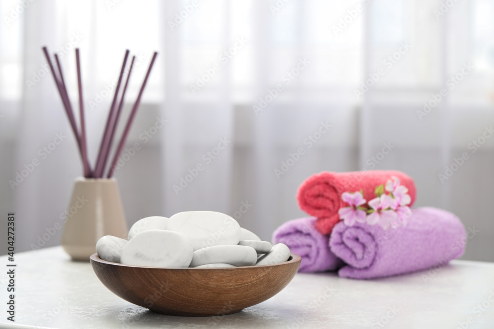 Spa stones, towels and reed freshener on white table indoors