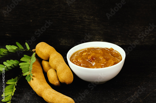 Tamarind juice in white bowl and tamarind fresh tropical fruit with leaf on black wooden background for cooking, dark tone.
