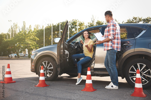 Instructor with clipboard and his student near car outdoors. Driving school exam photo