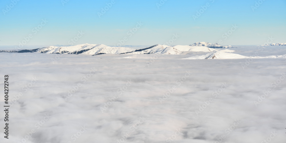 Sea of clouds in Winter, above Sinaia ski resort in Romania, with snow covered Carpathian mountain peaks in the distance. Temperature inversion, cloud inversion.	