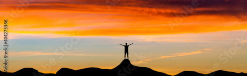 Silhouette tourists standing on top of a mountain peak, panoramic sunset views.The symbol represents the success of the business.