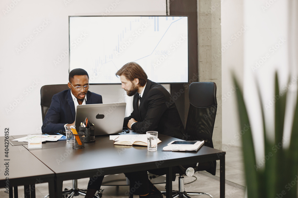 African man in a black suit. International partners. People sitting at the table with laptop. African man in a black suit. International partners. People sitting at the table with laptop.
