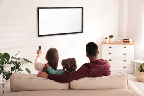 Family watching TV on sofa at home, back view
